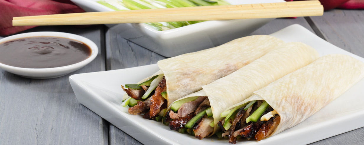 Chinese peking duck wrapped in pancakes with cucumber, spring onions and hoisin sauce