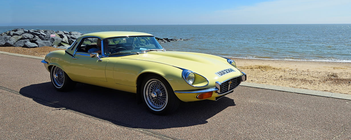 A yellow Jaguar E-Type driving along a coastal road with the sea in the background
