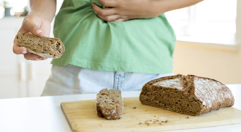 Close-up of a woman in a green top holding her stomach while standing over some brown bread