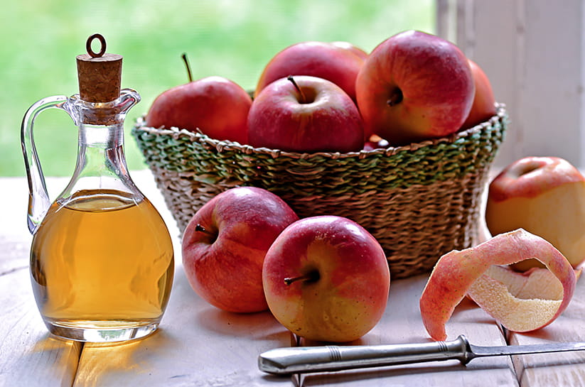 Apple cider vinegar next to a basket of apples