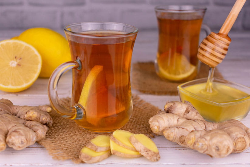 Two glass mugs of tea with slices of lemon, with fresh lemon, ginger and honey on the table around them