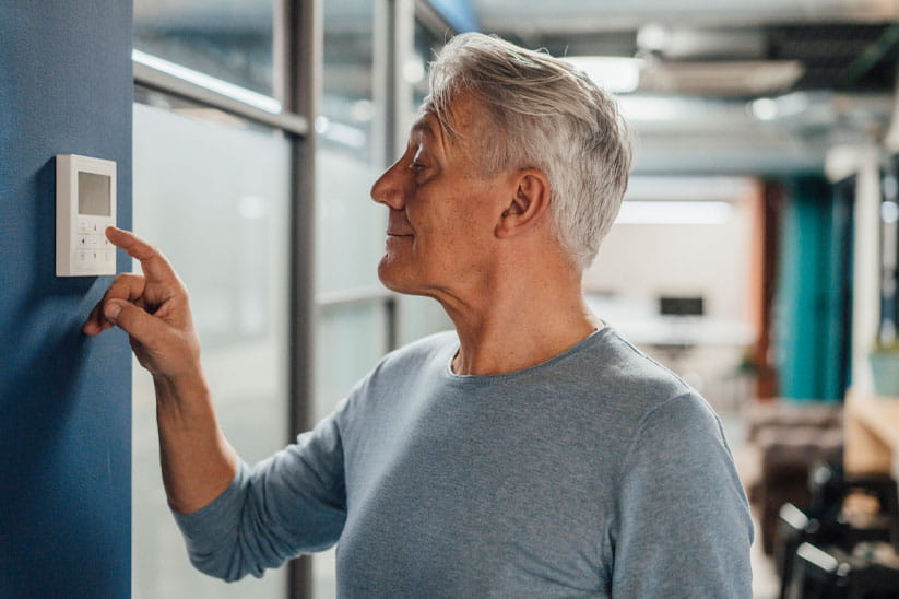 An older man adjusting a wall thermostat