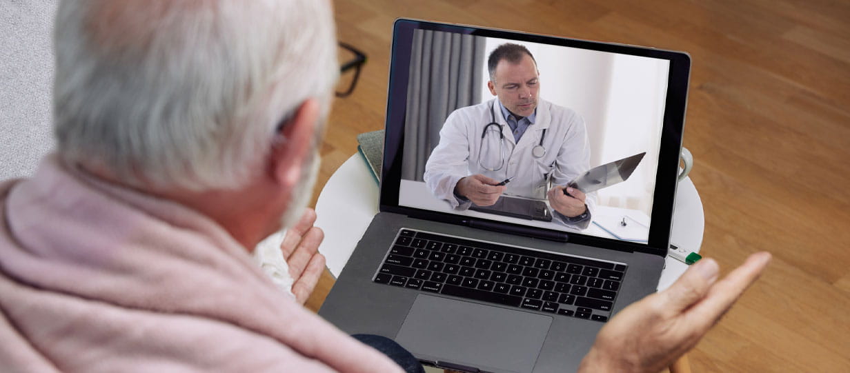 An older man consulting with a clinician on a laptop screen