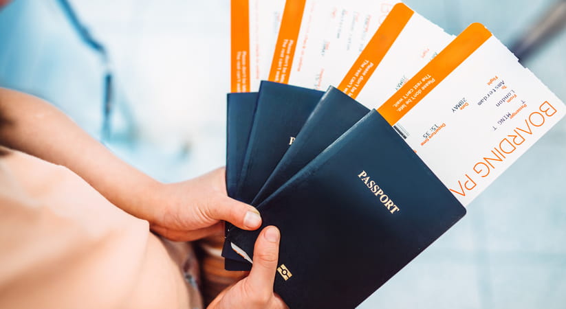 Close up of hands holding four blue passports with boarding passes