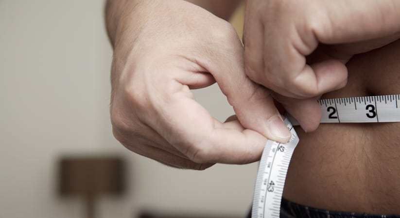 Close up of a man with no top on measuring his own waist