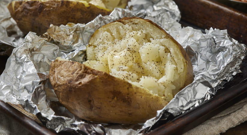 Close up of a baked potato with cheese inside on top of tin foil
