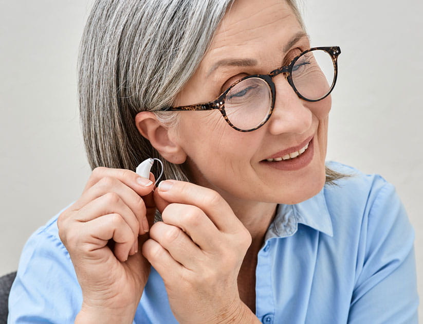  Mature woman wearing glasses about to put a hearing aid on