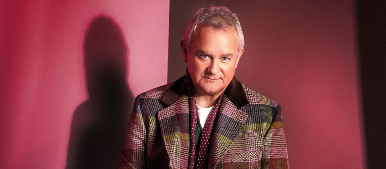 Head and shoulders shot of Hugh Bonneville facing the camera with a red background