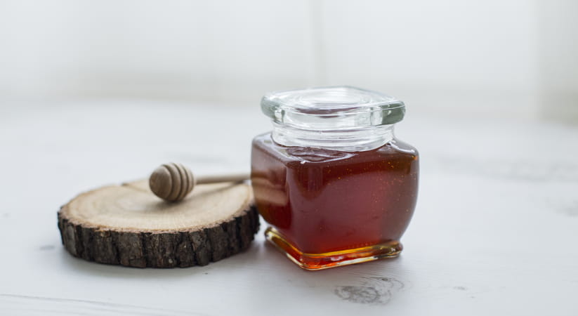 Close up of a jar of dark honey on a white table