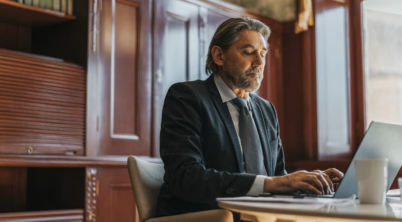 A middle aged man in a suit works on his laptop