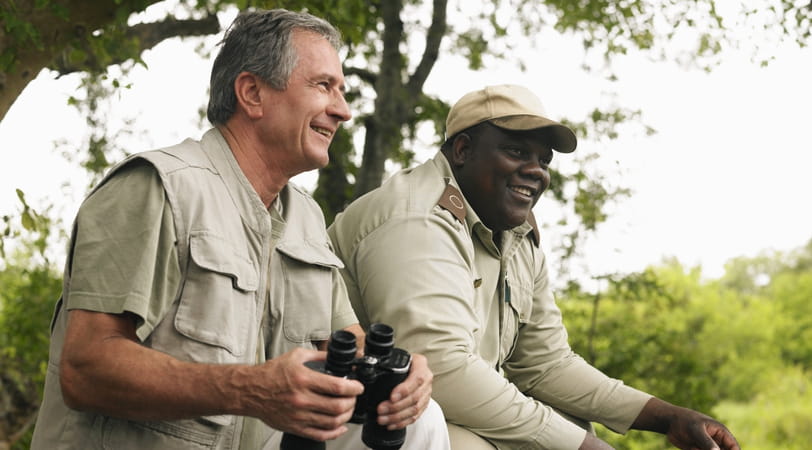 An older male tourist holding binoculars enjoys a safari with a guide