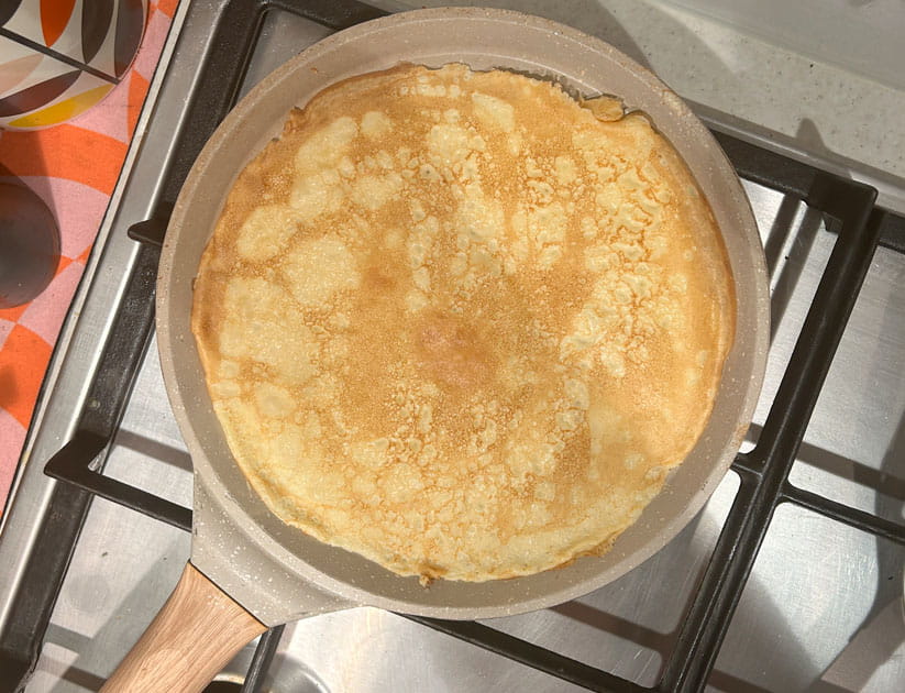 A golden crepe style pancake in a pan made using Delia's recipe