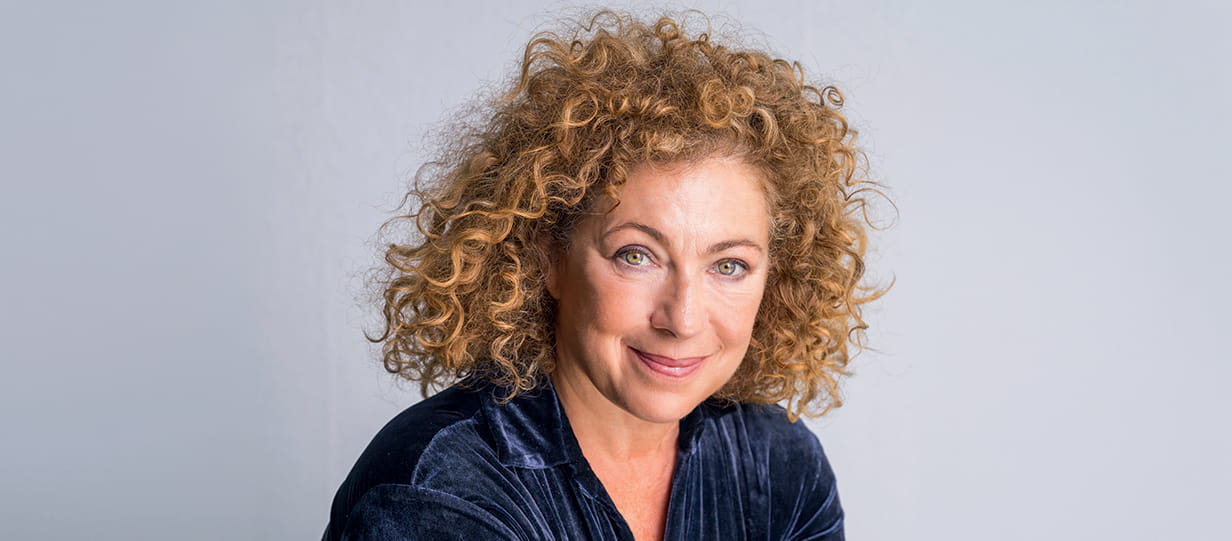 Portress of Alex Kingston wearing a black shirt against a grey background