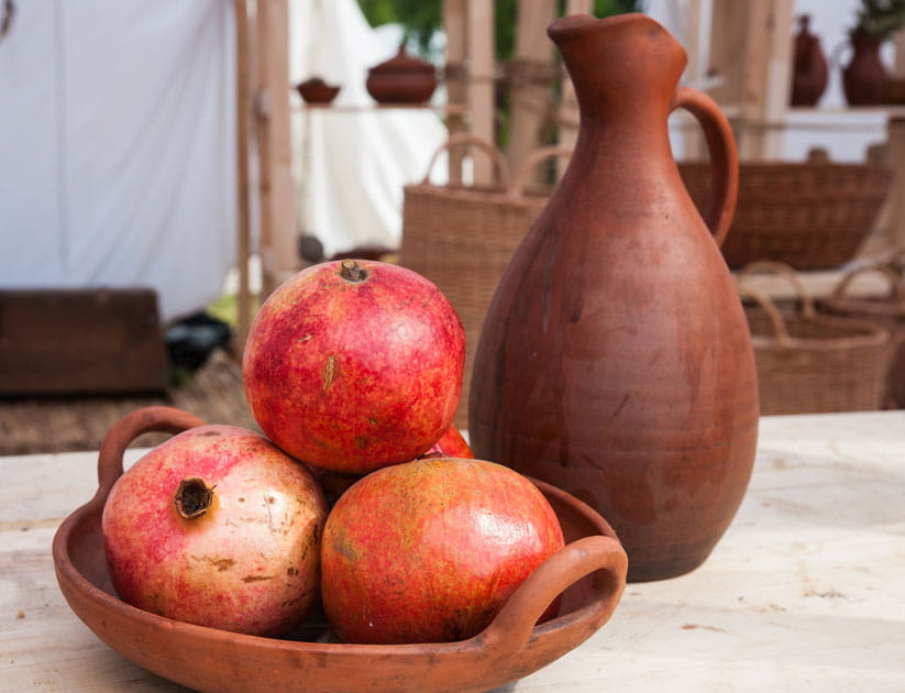 Still life of an earthenware bowl full or red pomegranate fruits and an earthenware pitcher of brown color. Wicker baskets in the background.