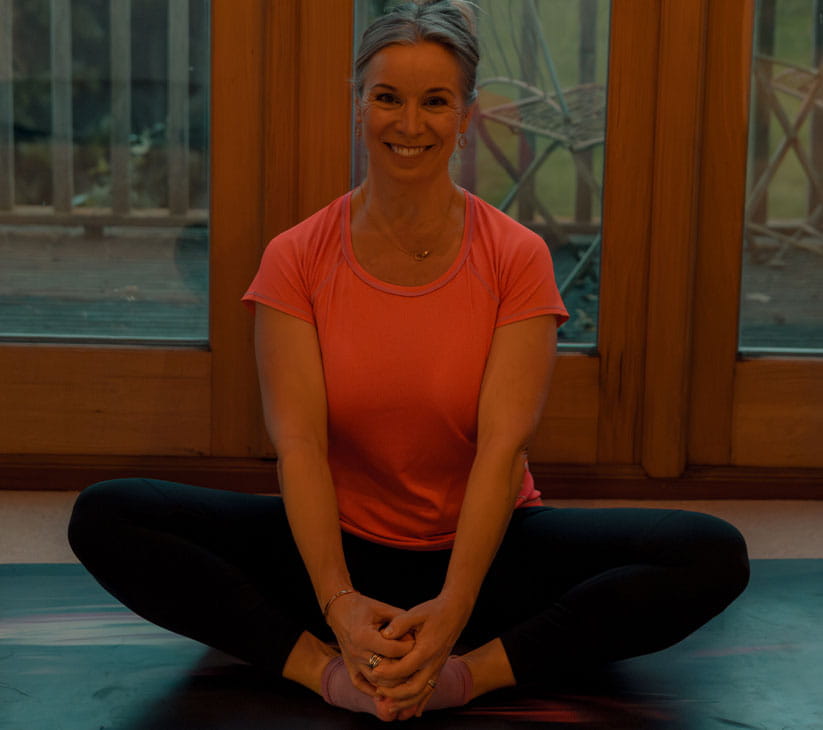 Author Sarah Denton on a yoga mat wearing an orange t-shirt in a seated pose