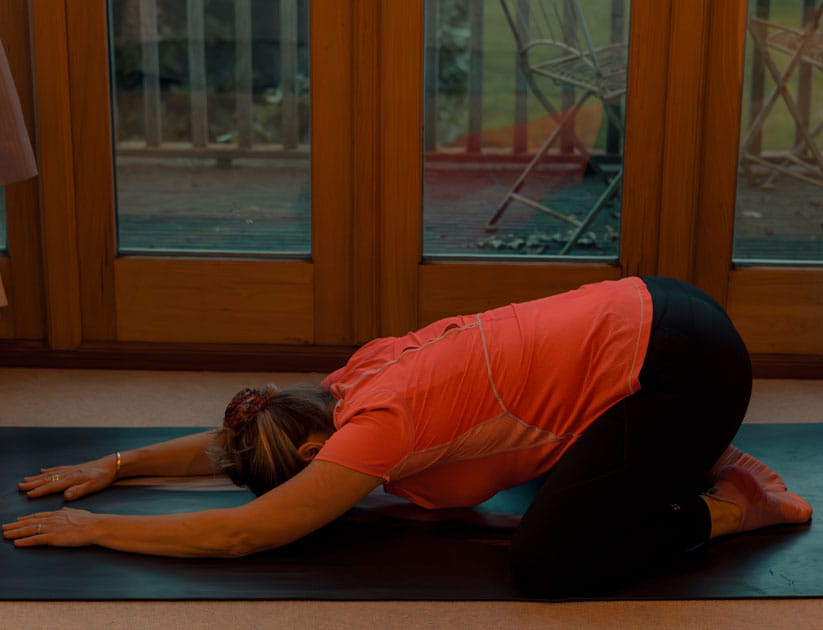 Author Sarah Denton on a yoga mat wearing an orange t-shirt in a child's pose yoga posture