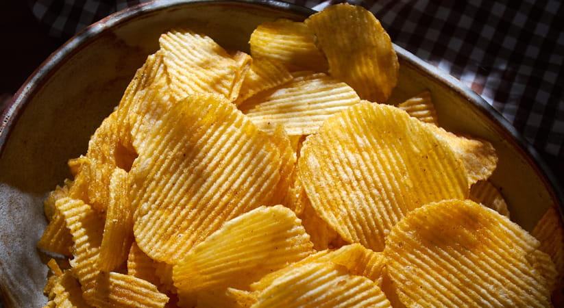 Close up of a bowl of crinkle cut crisps against a black background