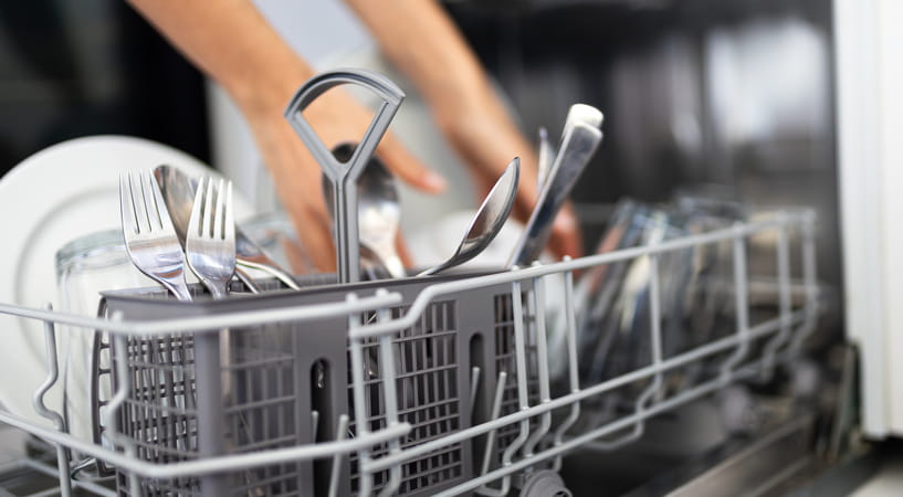Close up of a full cutlery tray in a dishwasher with two arms in the background