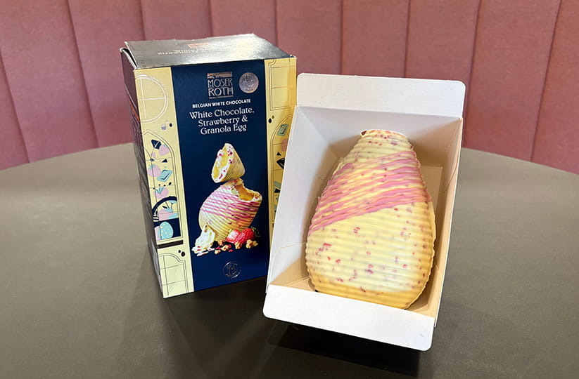 A Belgian white chocolate, strawberry and granola easter egg next to its packaging