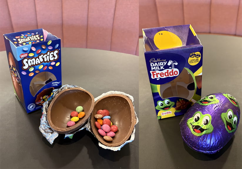 A Freddo Easter egg still in its foil, and an open Smarties Easter egg with Smarties inside, both sitting next to their packaging