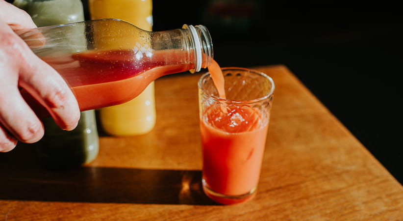 Close up of a hand pouring fruit juice from a bottle into a glass