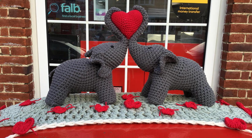Close up of the top of a postbox with two crochet elephants wrapping their trunks around a heart