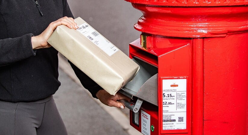 Close up of a person putting a parcel into the slot of a new postbox