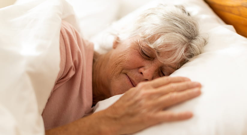 Close up of an older woman with short white hair sleeping on her side in bed 