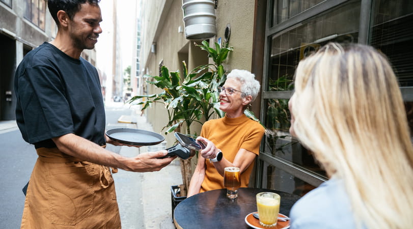 Two seated older women paying their bill to a standing waiter in a restaurant