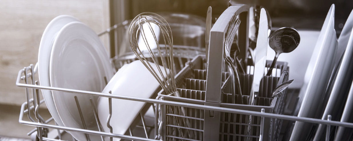 Front view of open automatic stainless steel built-in fully integrated top control dishwasher range machine with clean utensils, cutlery, glasses, dishes, plates inside in modern home kitchen