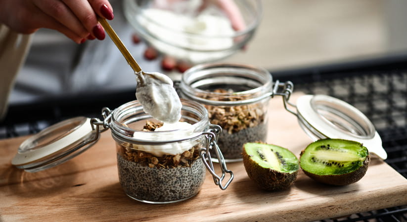 Close up of a hand spooning yogurt into a bowl of seeds on a wooden chopping board
