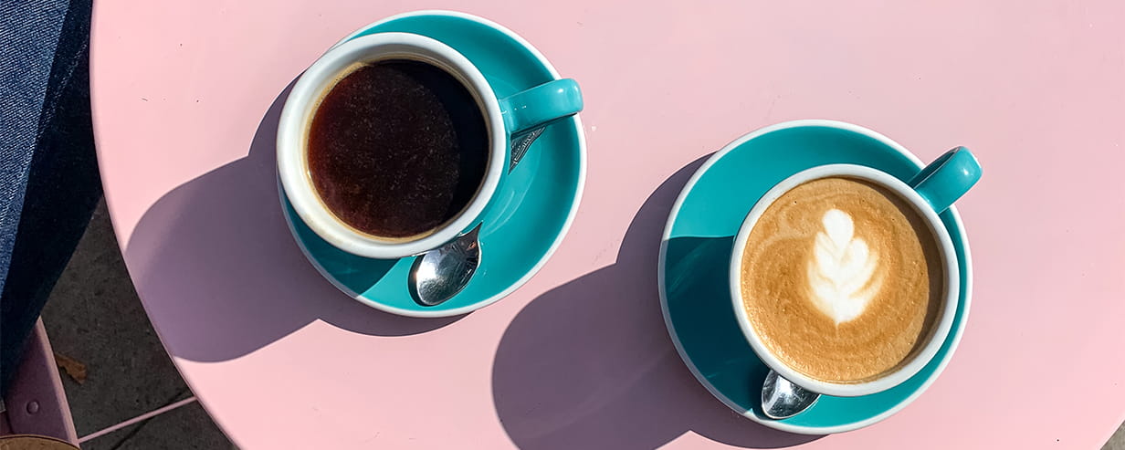 Morning coffee and tea in tiffany colour ceramic mugs with saucers on pink table. View from above