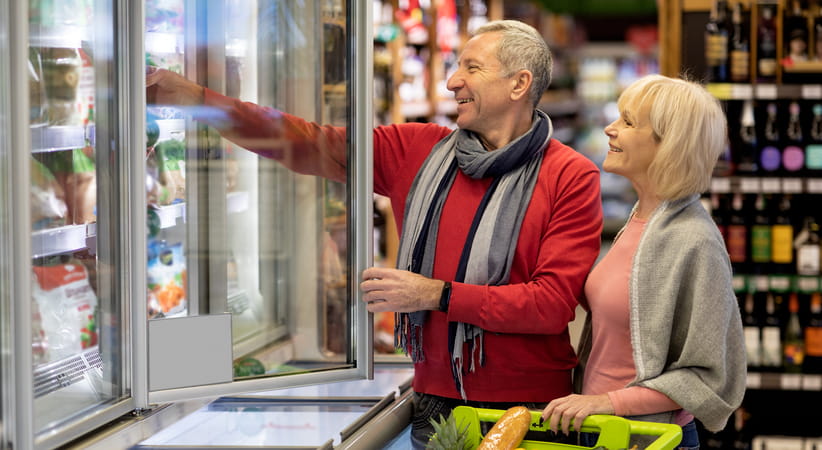 An older couple shop in the frozen section of a supermarket