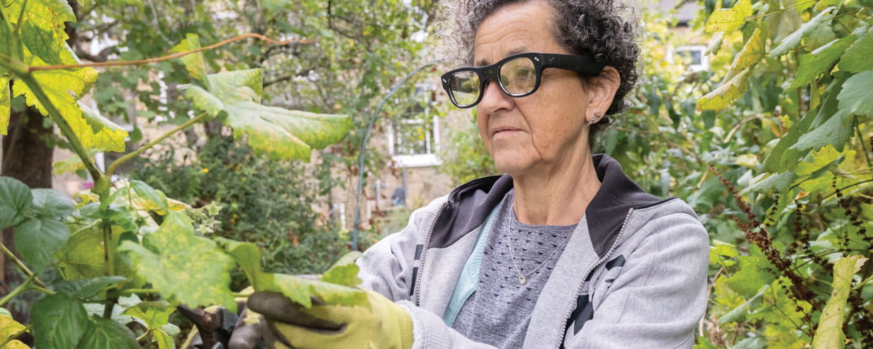 A mature woman gardening while wearing ai dementia glasses to assist with the task
