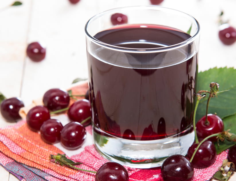 Fresh made cherry juice on wooden background, surrounded by fresh cherries