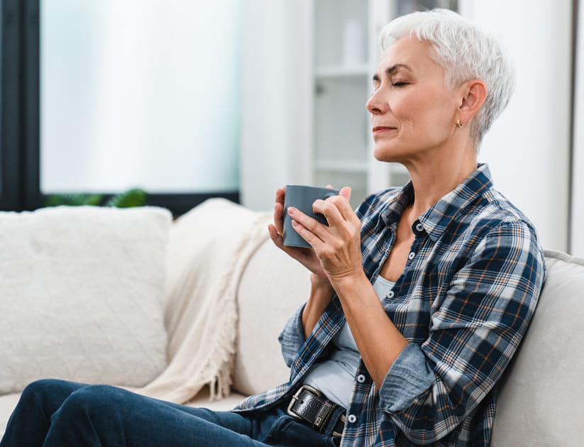 Chilling European mature woman in casual clothes relaxing with hot beverage in the living room