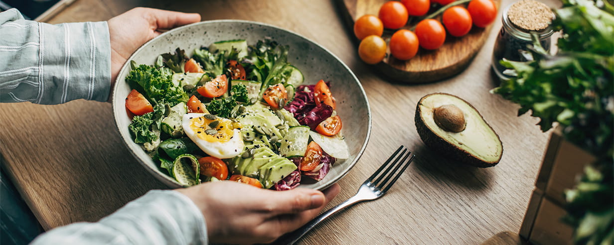 Woman mixing salad ingredients with wooden spoons in kitchen