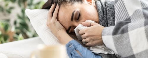 A woman lies on a sofa with a cold