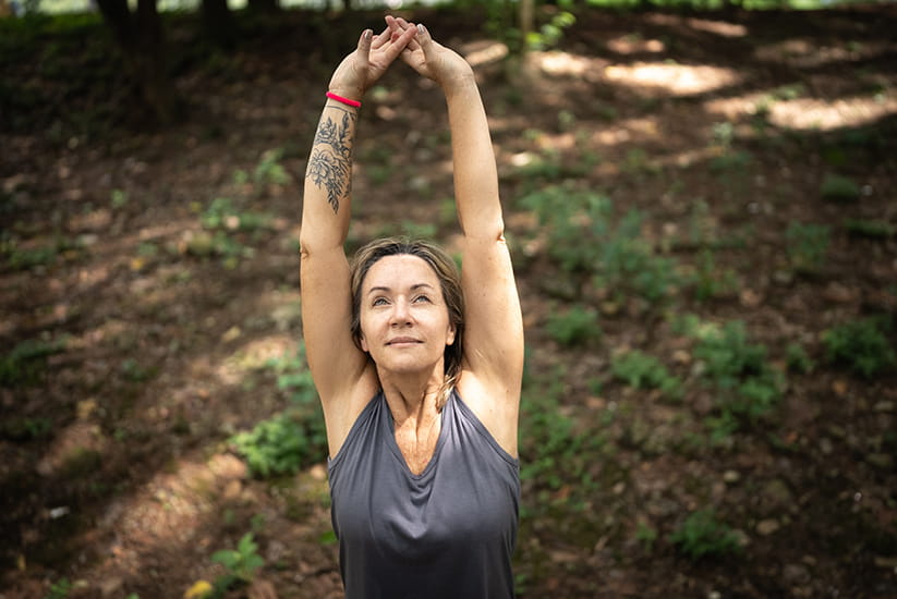 An older woman in a park stretching both arms above her head