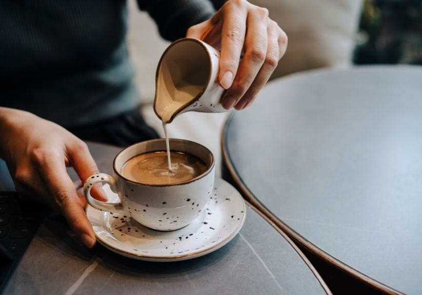 A person pours milk into a coffee into a cup on a saucer