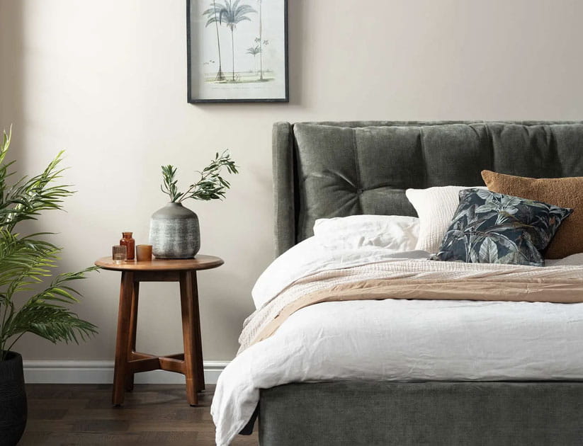 A fresh looking, spring themed bedroom with a green velvet bed-frame, coloured cushions and throw