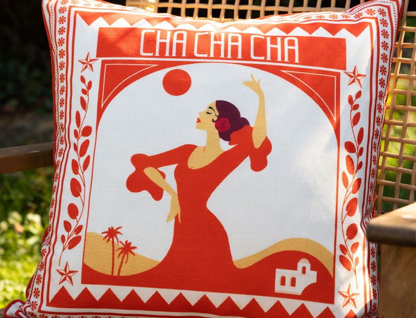 A bright cushion with red on white print of a stylised Spanish lady and geometric designs and the words 'Cha cha cha' at the top