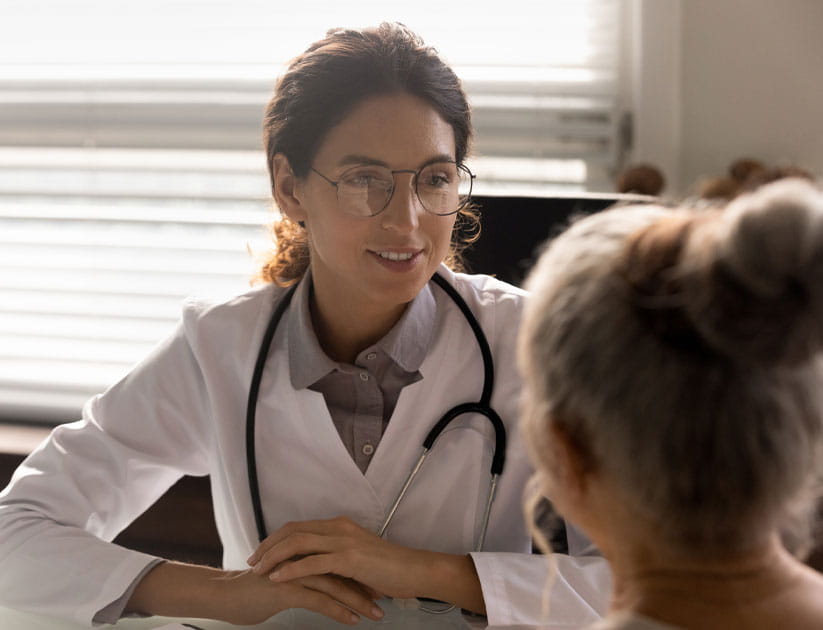 Close up smiling female gp wearing glasses consulting mature patient during appointment