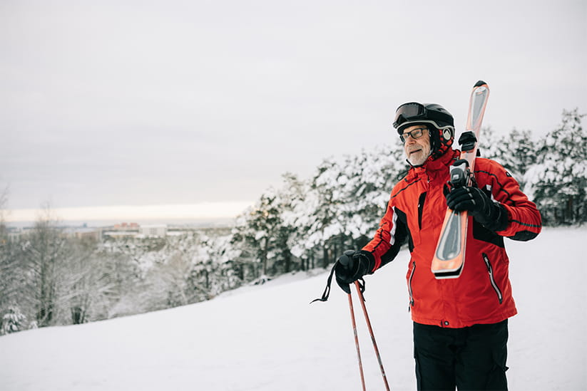 Active senior man walks with skis on his shoulder