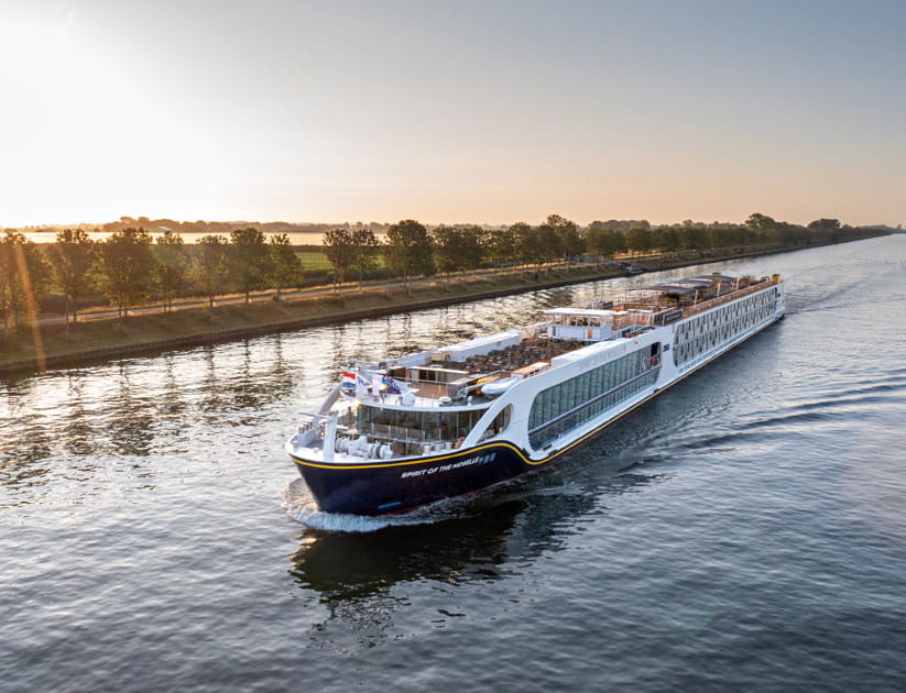 Saga's river cruise ship The Spirit of the Moselle travelling along a river with rays of sunshine coming in from the left