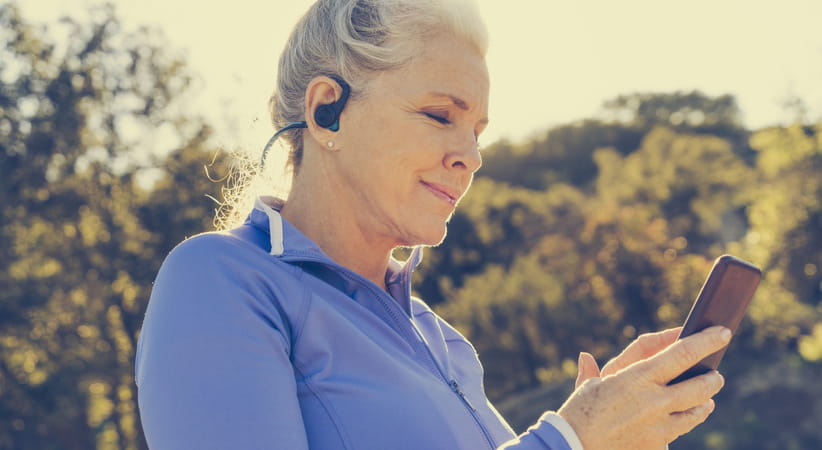 Older woman in a blue top checking her phone while out running