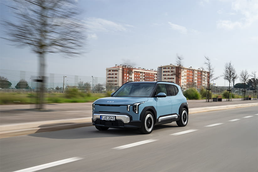 A light blue Kia EV2 driving along a road