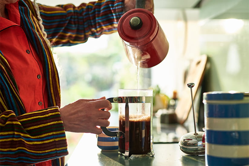 An older person pouring water from a kettle into a cafetiere