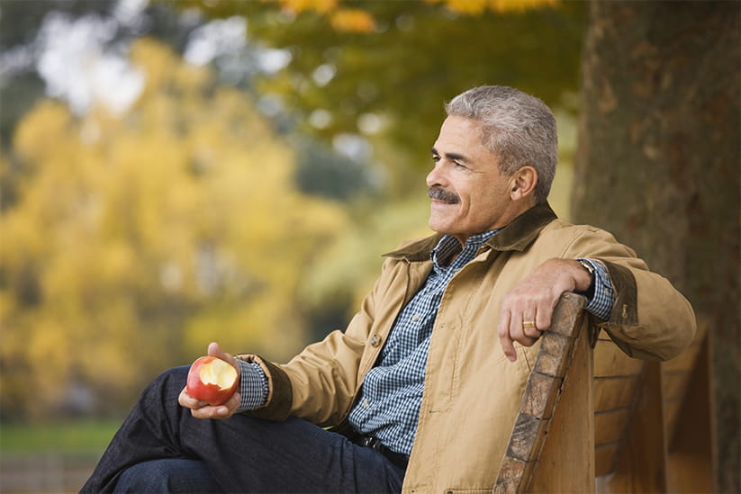 Older man eating apple on park bench