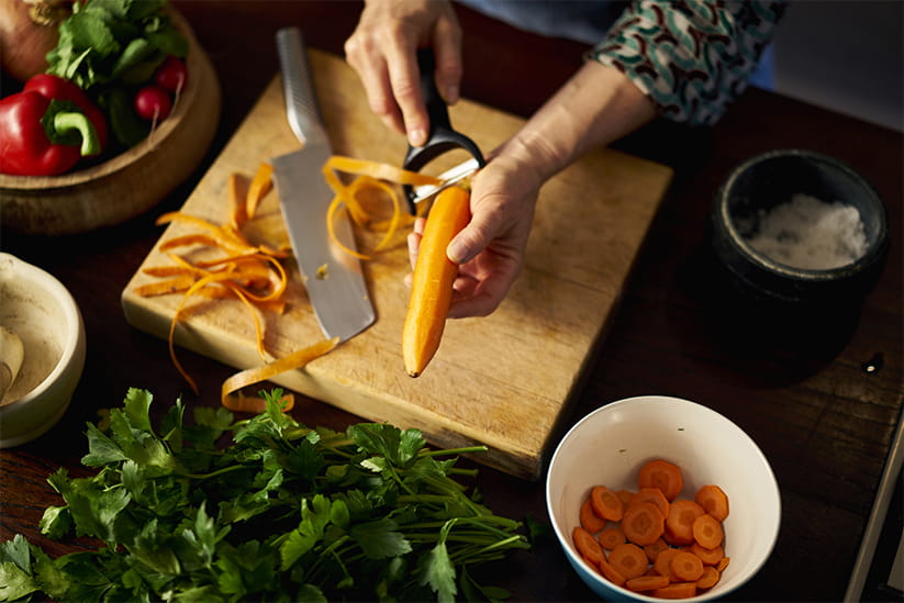 An older woman peeling carrots over a wooden chopping board